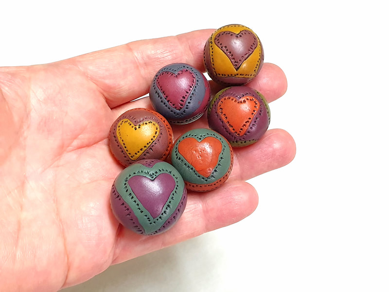 Hollow round polymer clay beads with a heart pattern, made by comprising pieces of clay in various colors together.