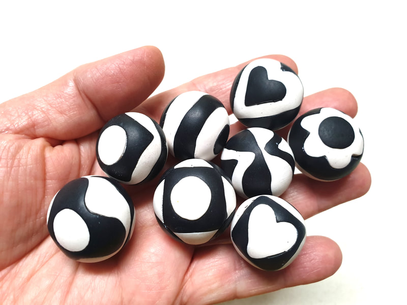 Hollow round polymer clay beads made by comprising pieces of clay in black and white in various patterns.